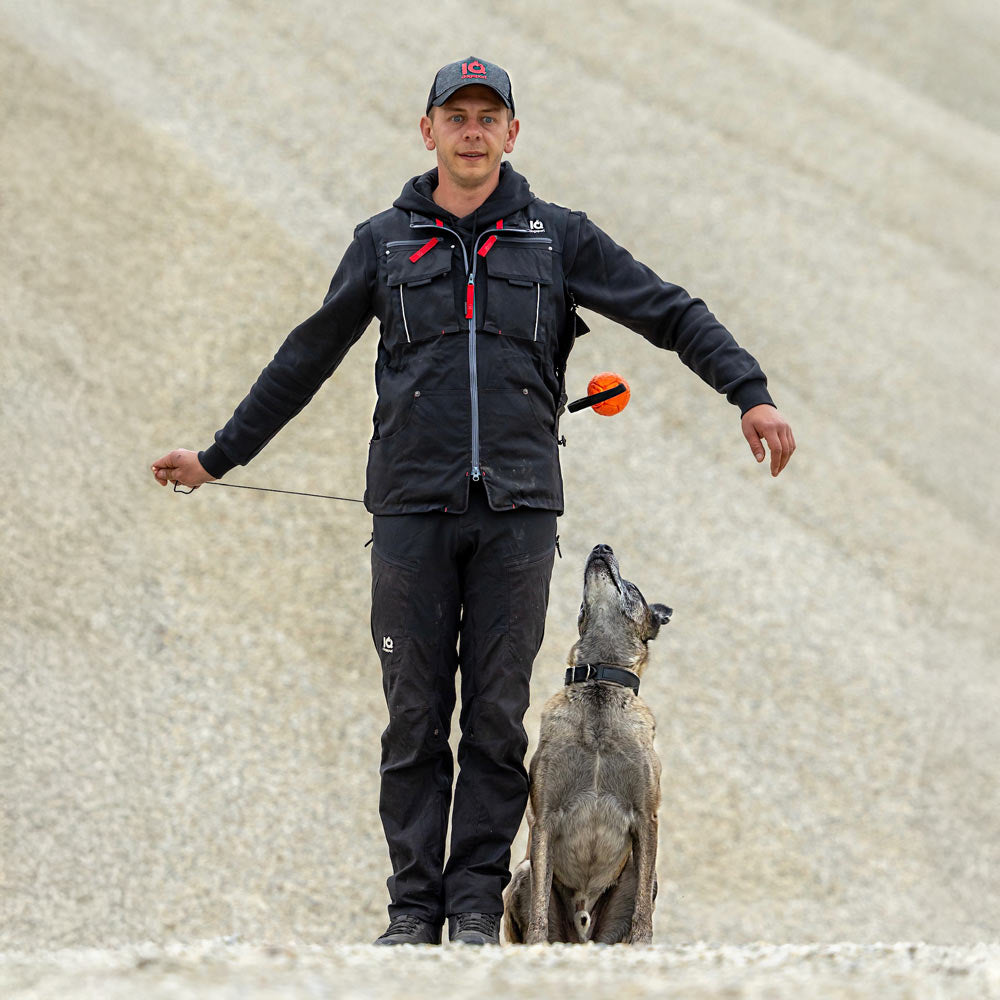 Hundeführer gibt einen Ball seitlich an der Weste frei, während der Hund aufmerksam hochschaut