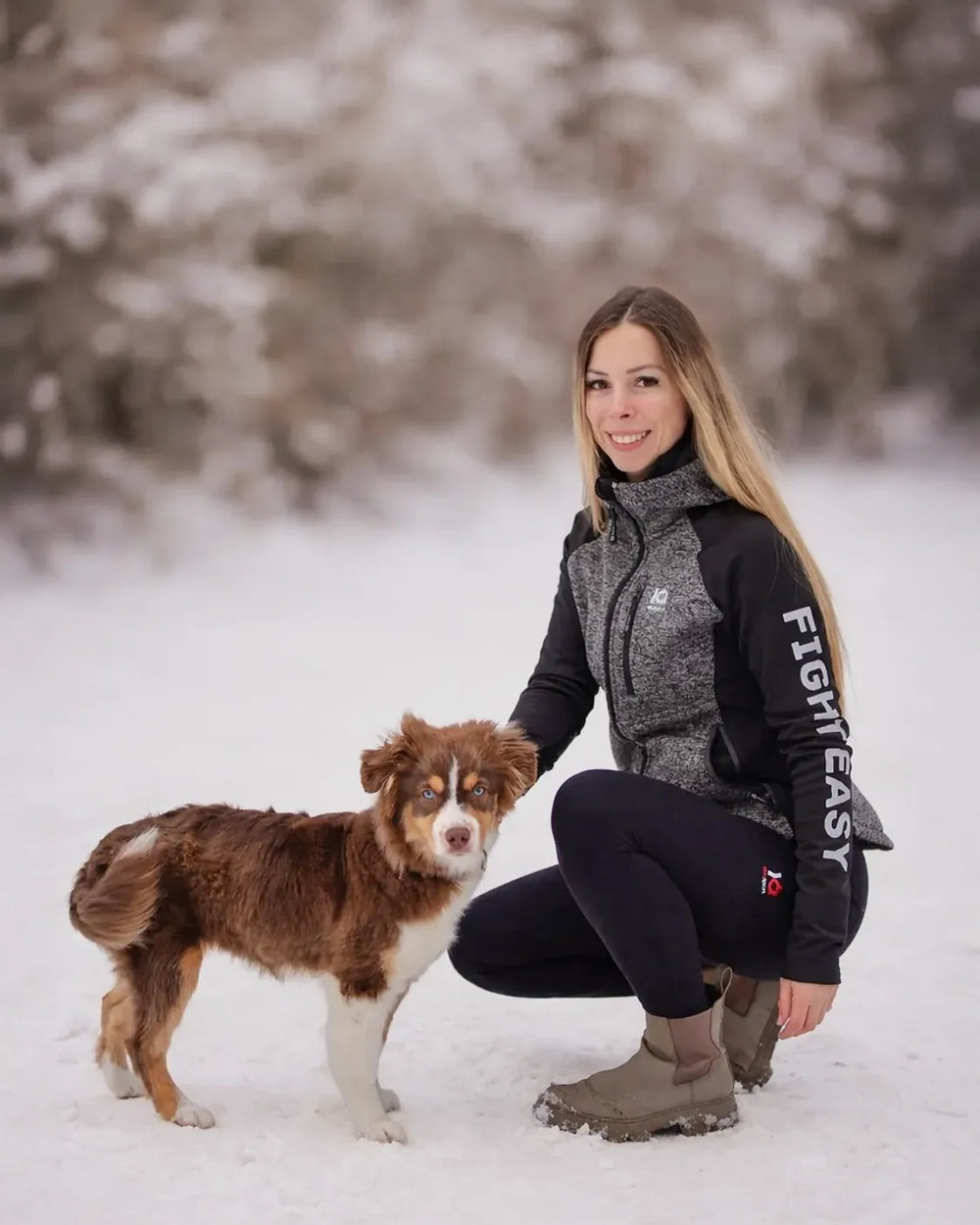 Frau im grau-schwarzen IQ Damen-Zip-Hoodie mit einem Aussie im Schnee