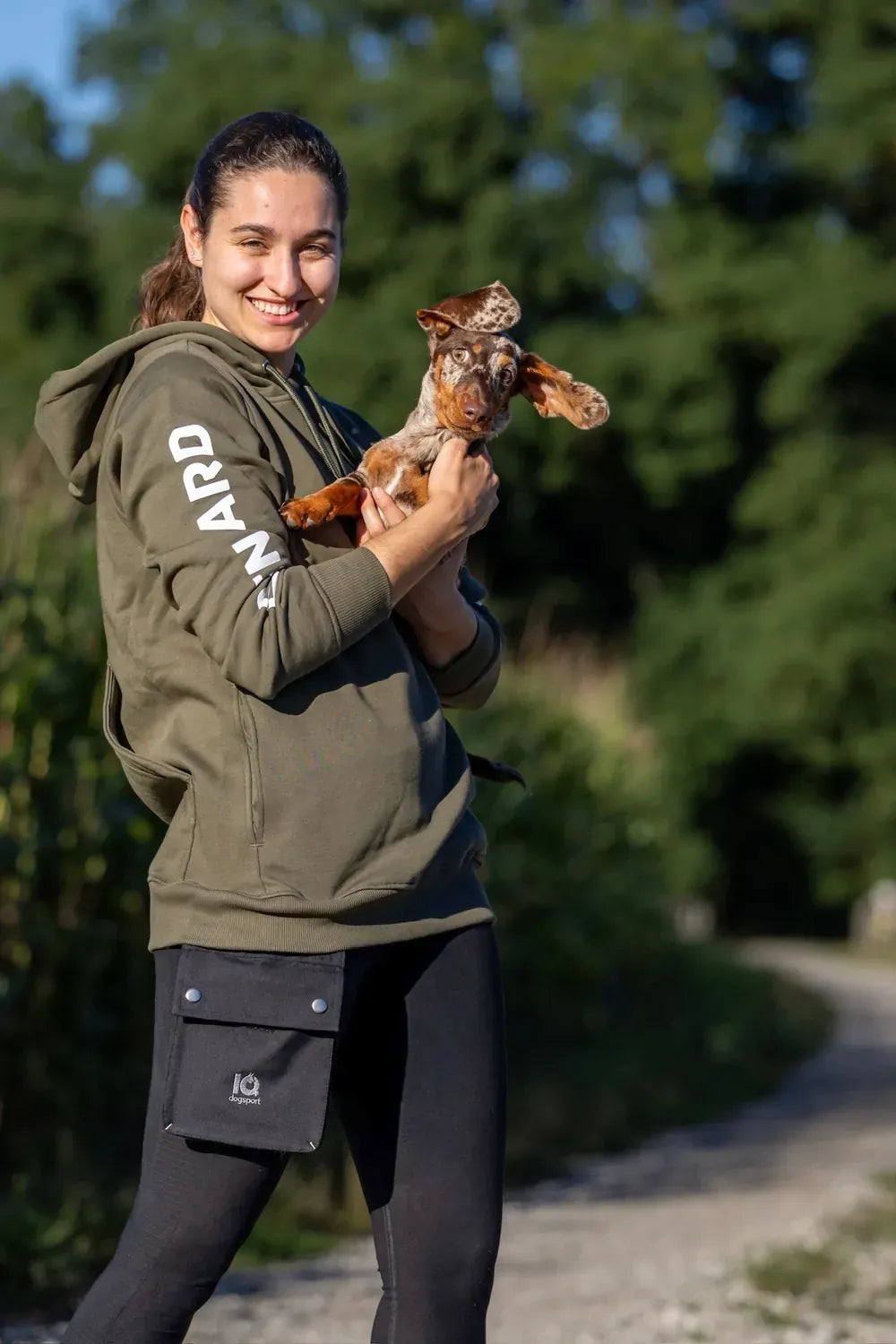 Olivfarbener Hoodie mit seitlich befestigter IQ modularer Futtertasche; Frau hält einen Dackel